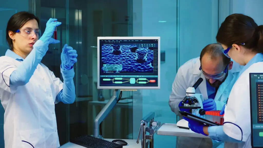 senior chemist analysing blood sample while coworkers discussing